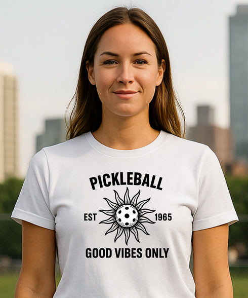 Woman wearing a white t-shirt with pickleball design and text, standing outdoors with a cityscape background.